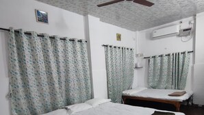 Une chambre d’hôtel avec deux lits simples, un ventilateur de plafond, un appareil de climatisation et des rideaux à motifs.