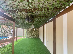 Un pasillo con césped artificial verde, techo de madera con plantas colgantes y un revestimiento mural con diseño.