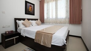 A neatly made bed with a white comforter and beige pillows, a brown throw blanket, and a framed floral painting above it. - Delightful Trizen 1-bedroom apartment with AC in Colombo 02 (Colombo 02)