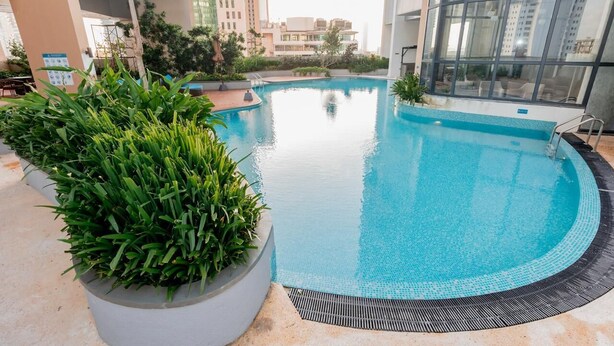 A swimming pool with a tiled edge, surrounded by greenery and modern buildings. - Delightful Trizen 1-bedroom apartment with AC in Colombo 02 (Colombo 02)