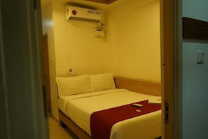 A hotel room with a bed, a bedside table, a wall-mounted air conditioner, and a door.