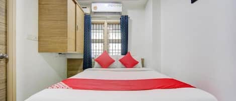 A hotel room with a bed, a wardrobe, a window with curtains, and an air conditioning unit.
