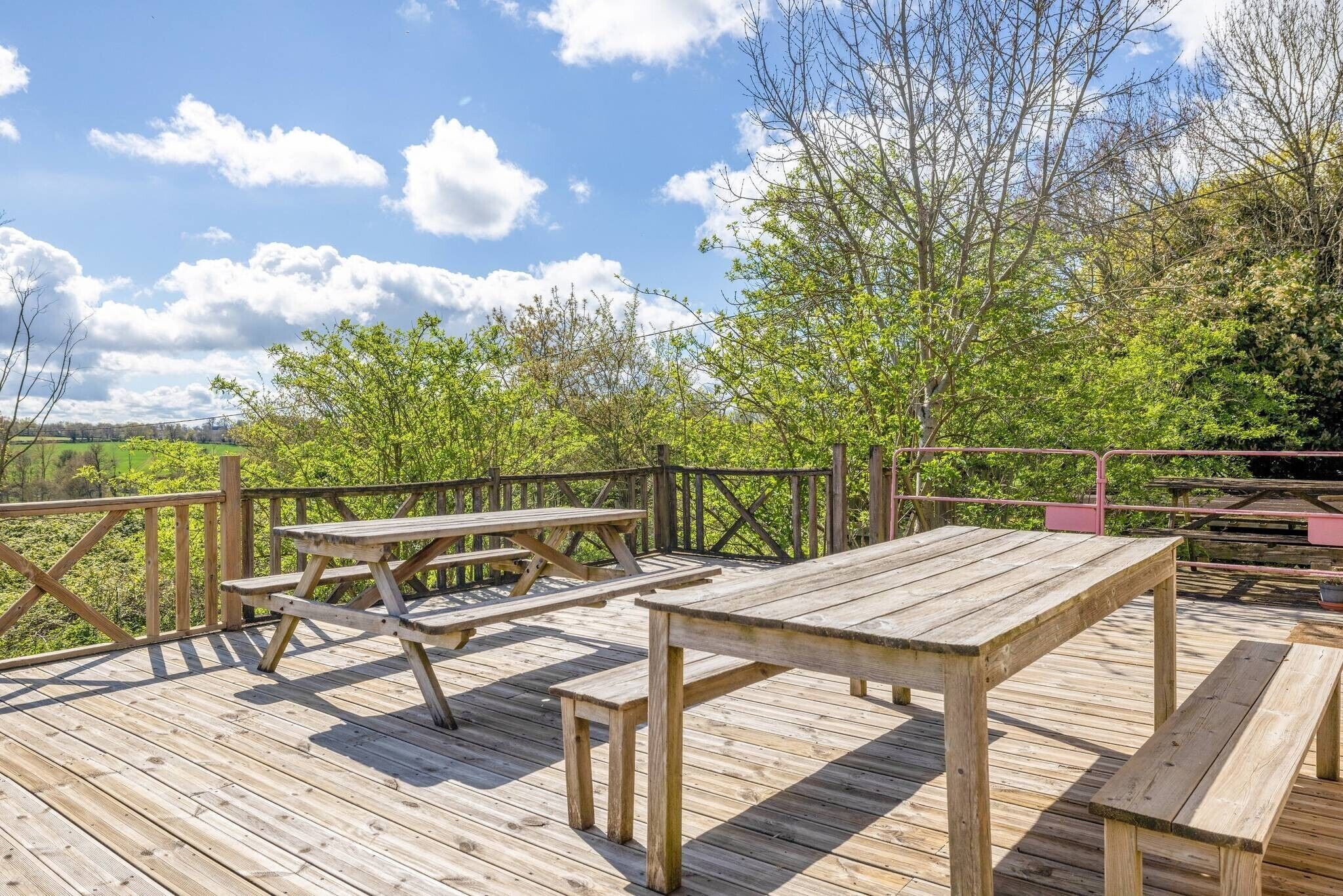 A wooden deck with picnic tables and a railing overlooking a green landscape.