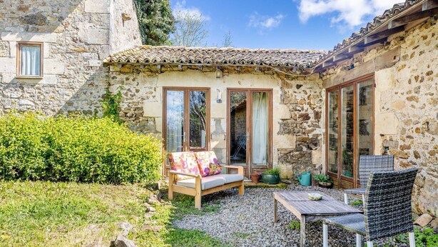A stone building with a patio area, a wooden bench, a table, and chairs. - Holiday Home “Gîte Des Hiboux” with Shared Pool, Private Terrace & Wi-Fi (Sanxay)