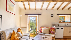 A cozy living room with a sofa, armchair, wooden table, and a view of the garden through a door. - Holiday Home “Gîte Des Hiboux” with Shared Pool, Private Terrace & Wi-Fi (Sanxay)