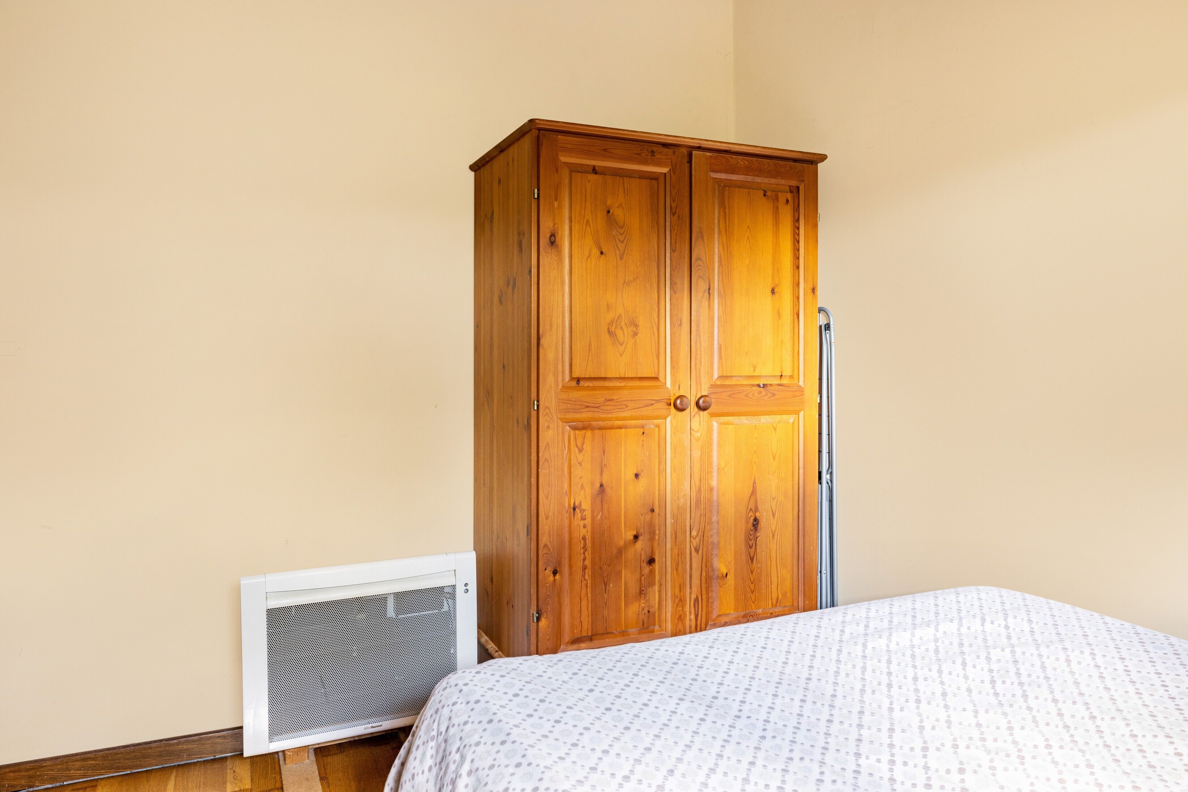 Un dormitorio con un armario de madera, una cama con cubrecama estampado y un equipo de aire acondicionado instalado en la pared.
