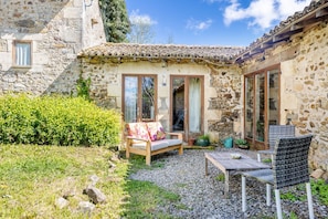 Un bâtiment en pierre doté d’une terrasse, d’un banc en bois, d’une table et de chaises.