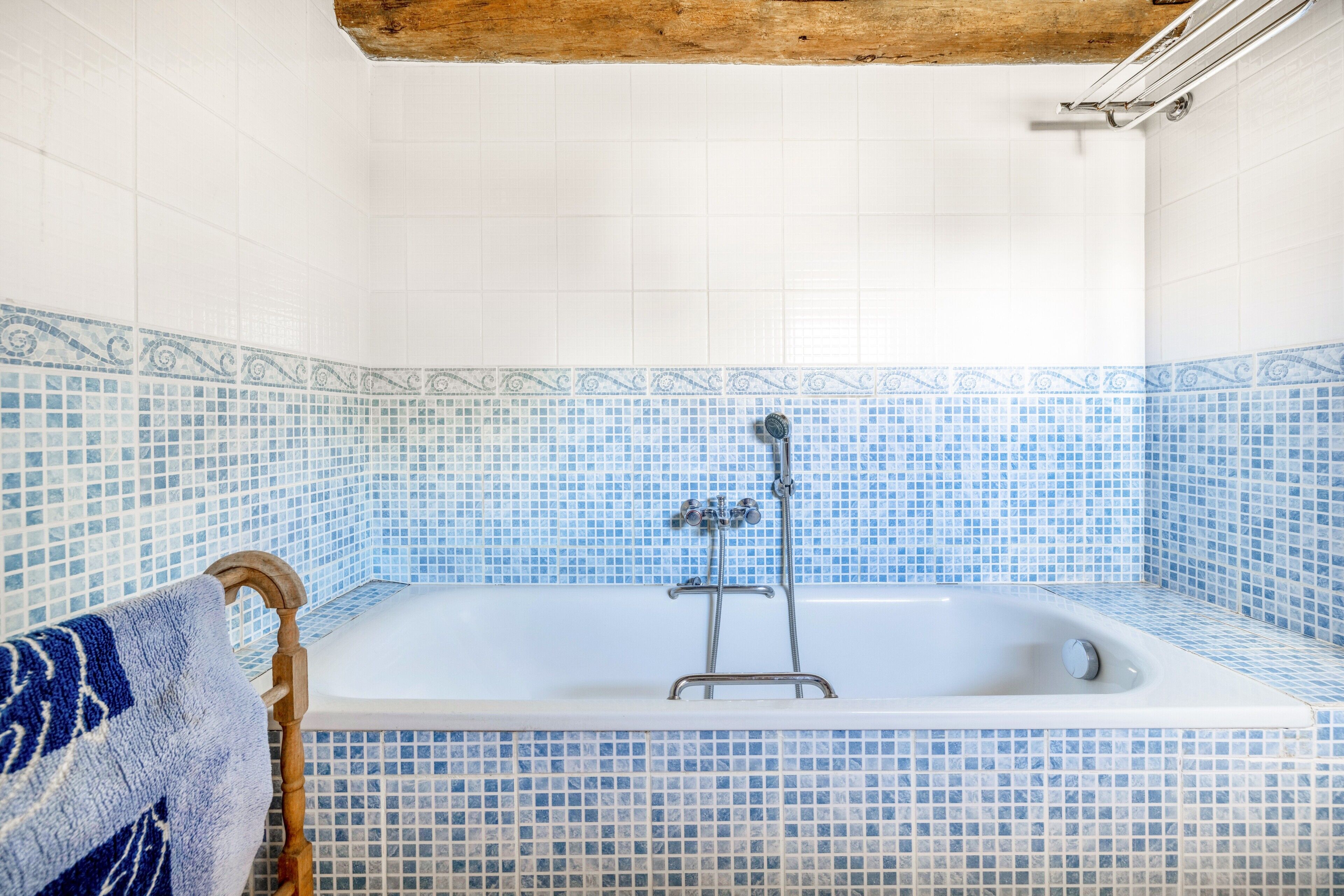 Un baño con bañera, paredes de azulejos y un perchero de madera.