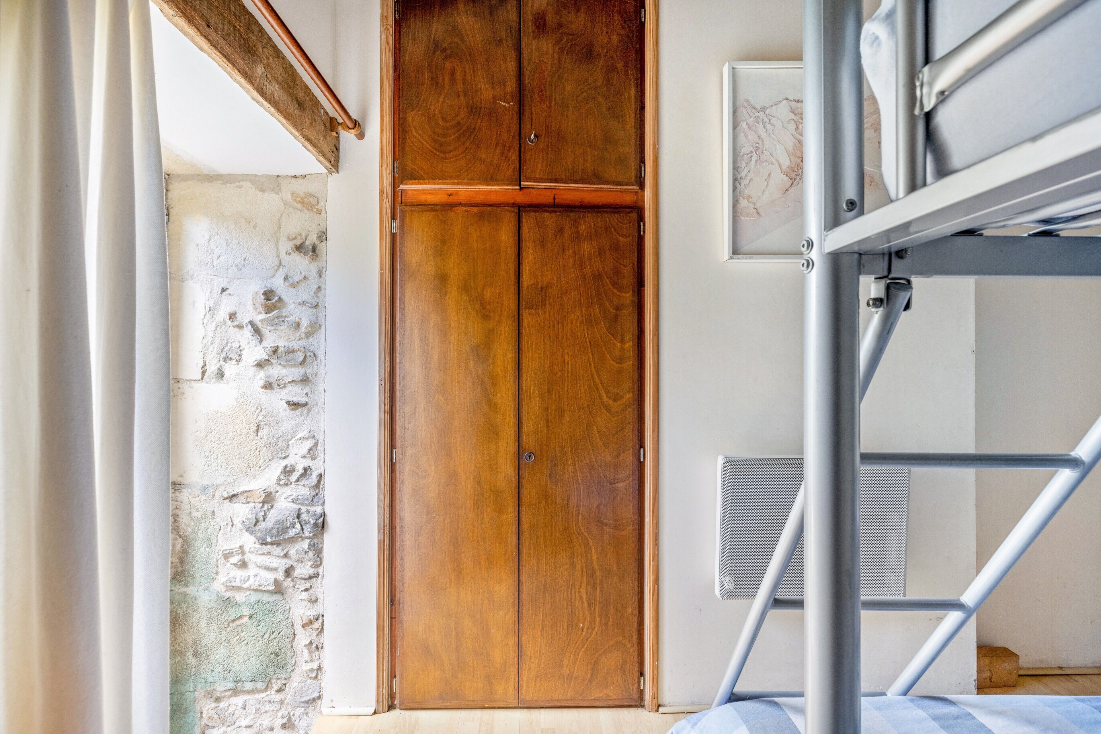 Ein Stockbett mit einem Holzschrank, einer Steinsäule und einem Fenster.