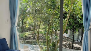 A modern room with a large sliding glass door leading to a garden. There is a blue sofa and a small table with a mat. - Tropical Fruit Garden Homestay (2 Bao Loc)