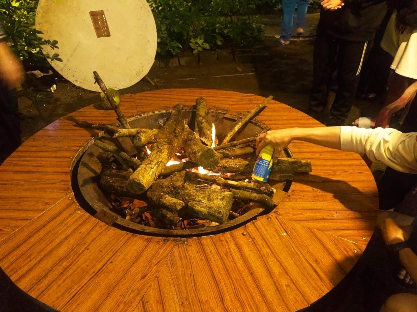 Une table ronde en bois, avec un foyer au centre, entourée de bûches.