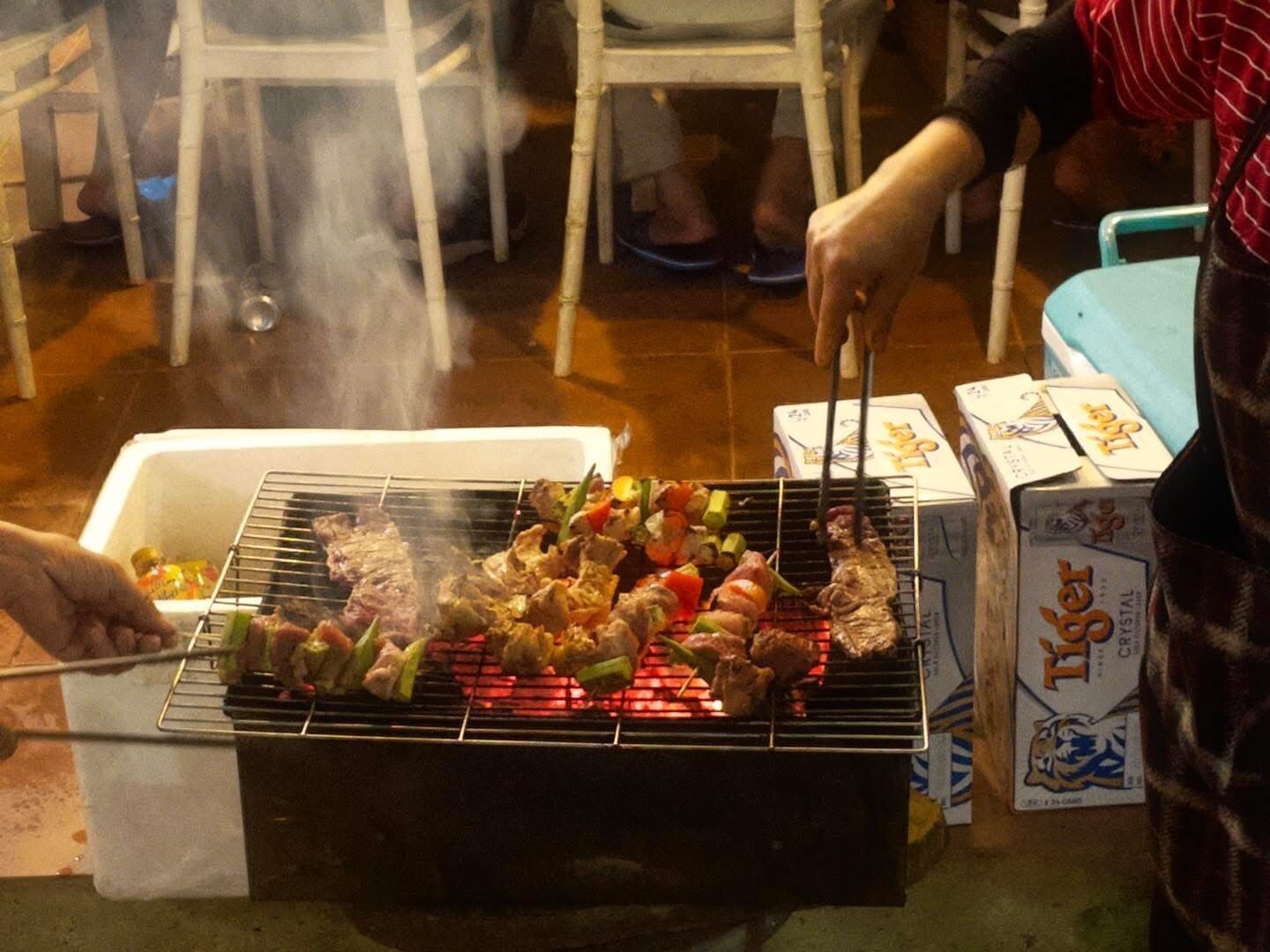 Una parrilla con brochetas de carne y verduras cocinándose al aire libre.