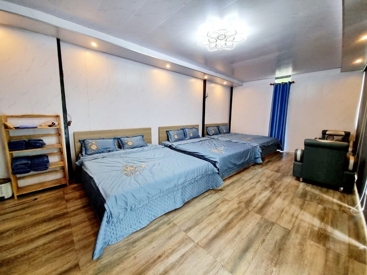 Une chambre avec deux lits, un plancher en bois, une étagère avec des vêtements pliés et une chaise.