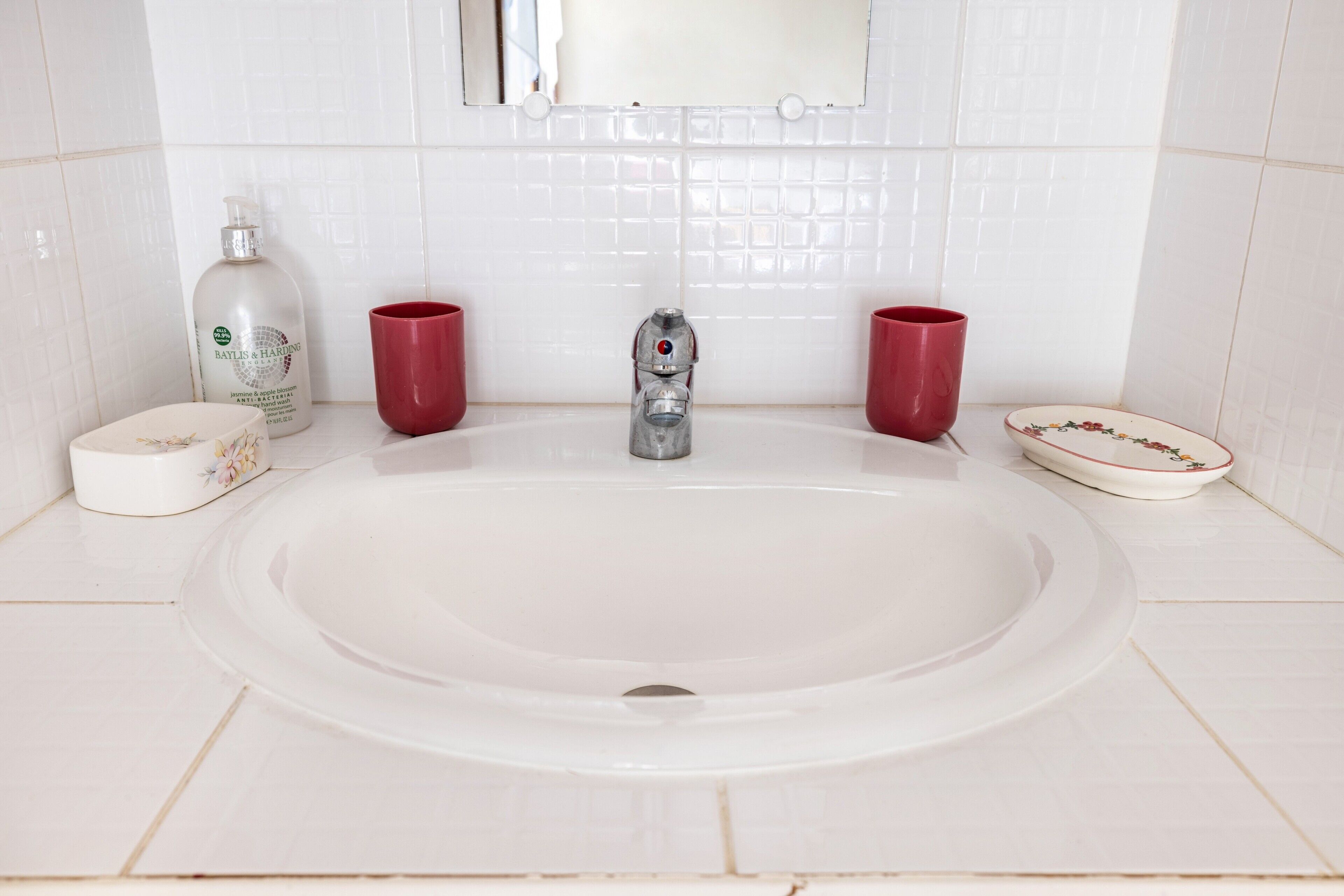 A bathroom with a white sink, a mirror, a red faucet, and a red cup.