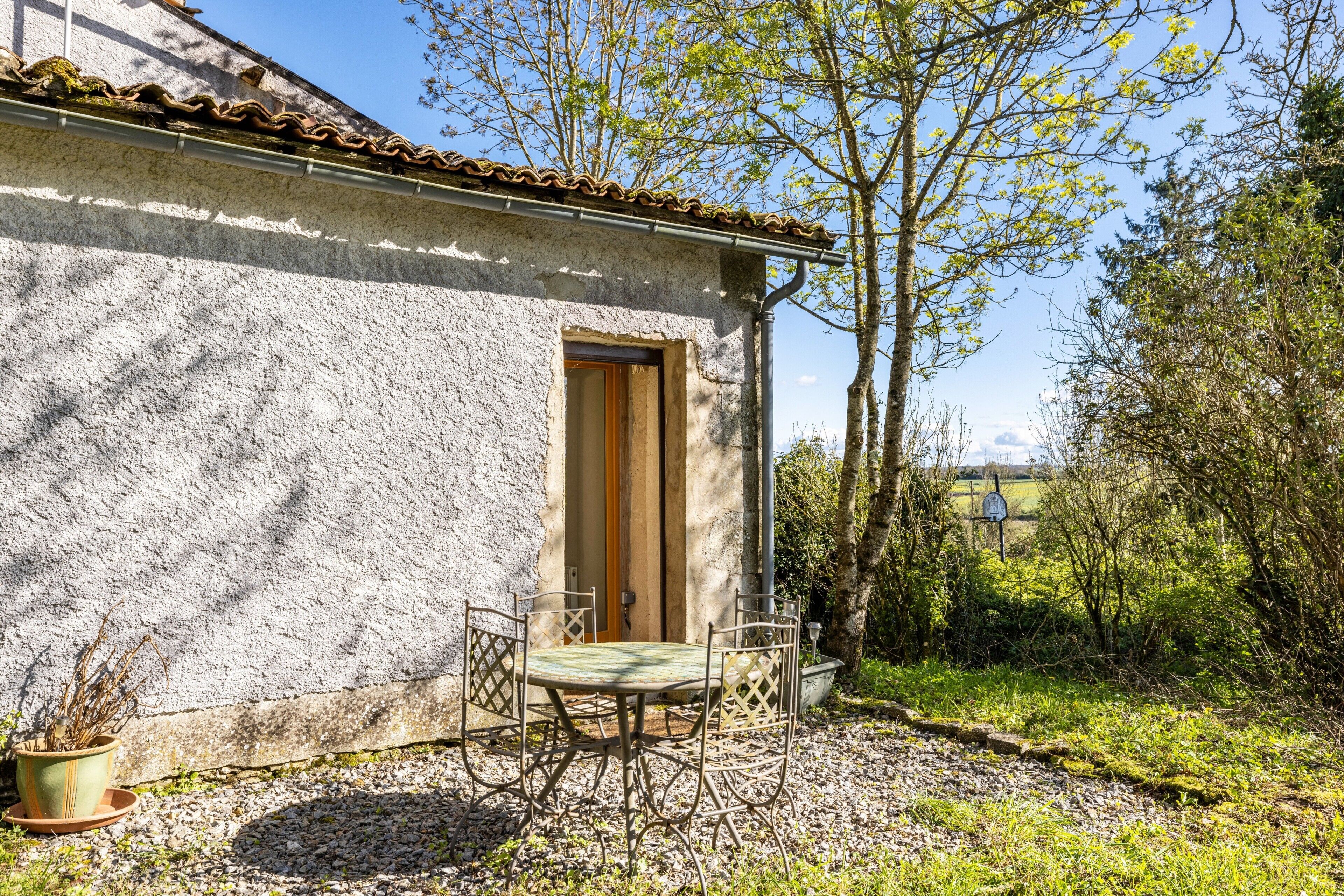 Un bâtiment rustique avec une porte, une petite table entourée de chaises et une plante en pot.