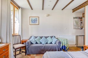 A room with a sofa, a chair, a bed, a wooden cabinet, a radiator, and a map on the wall.
