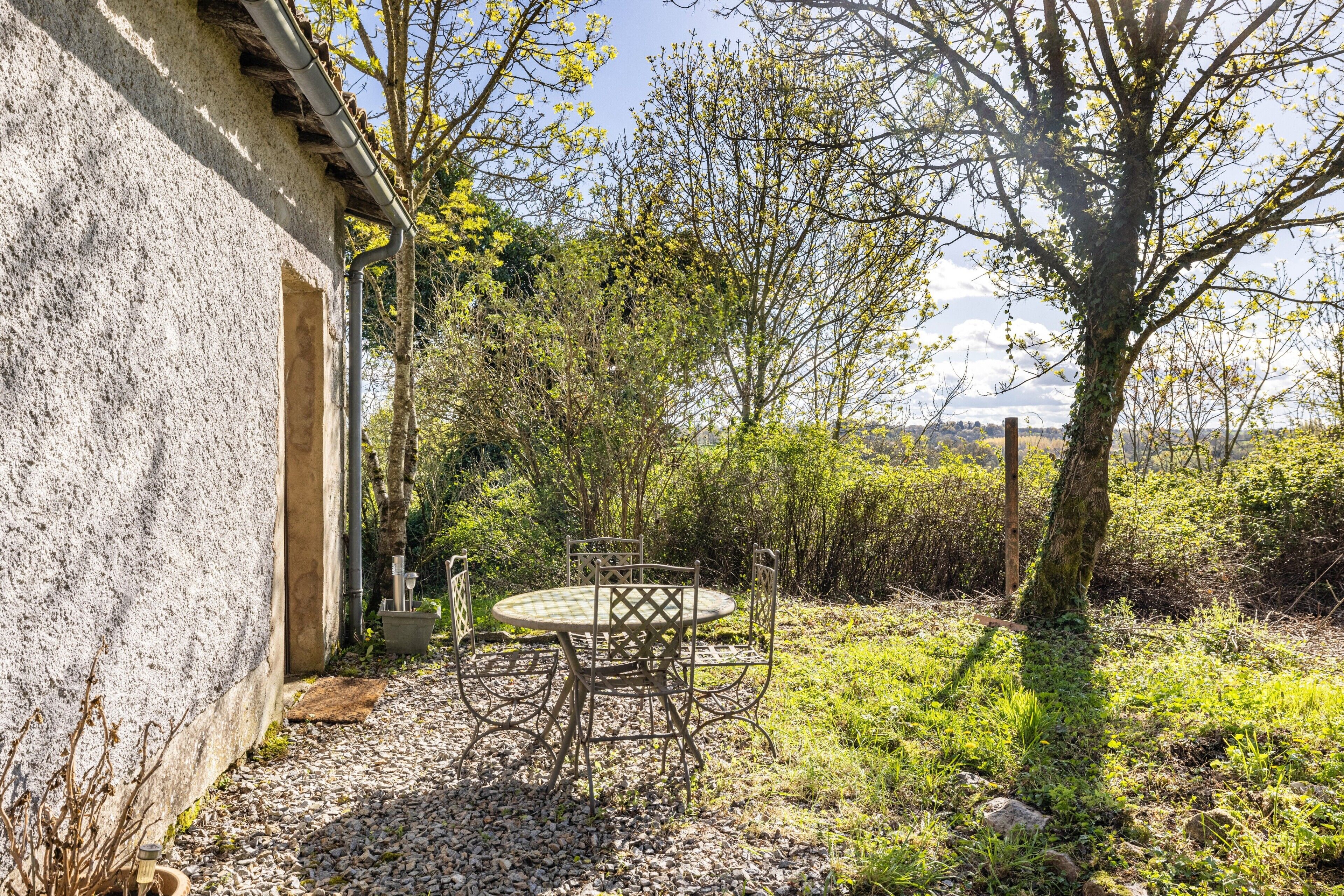 An outdoor patio with a table and chairs, surrounded by vegetation and a building.