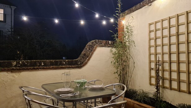 An outdoor dining area with a table set for two, surrounded by metal chairs, under string lights. - City Centre, River views, Sleeps 5, Free Parking (Canterbury)