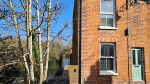 A brick building with a river, a green door, and a window with shutters. - City Centre, River views, Sleeps 5, Free Parking (Canterbury)