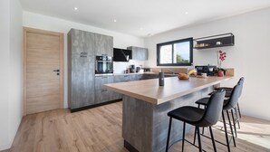 A modern kitchen with a central island, bar stools, and a built-in oven. - Newly Built House for Rent! (Plouescat)