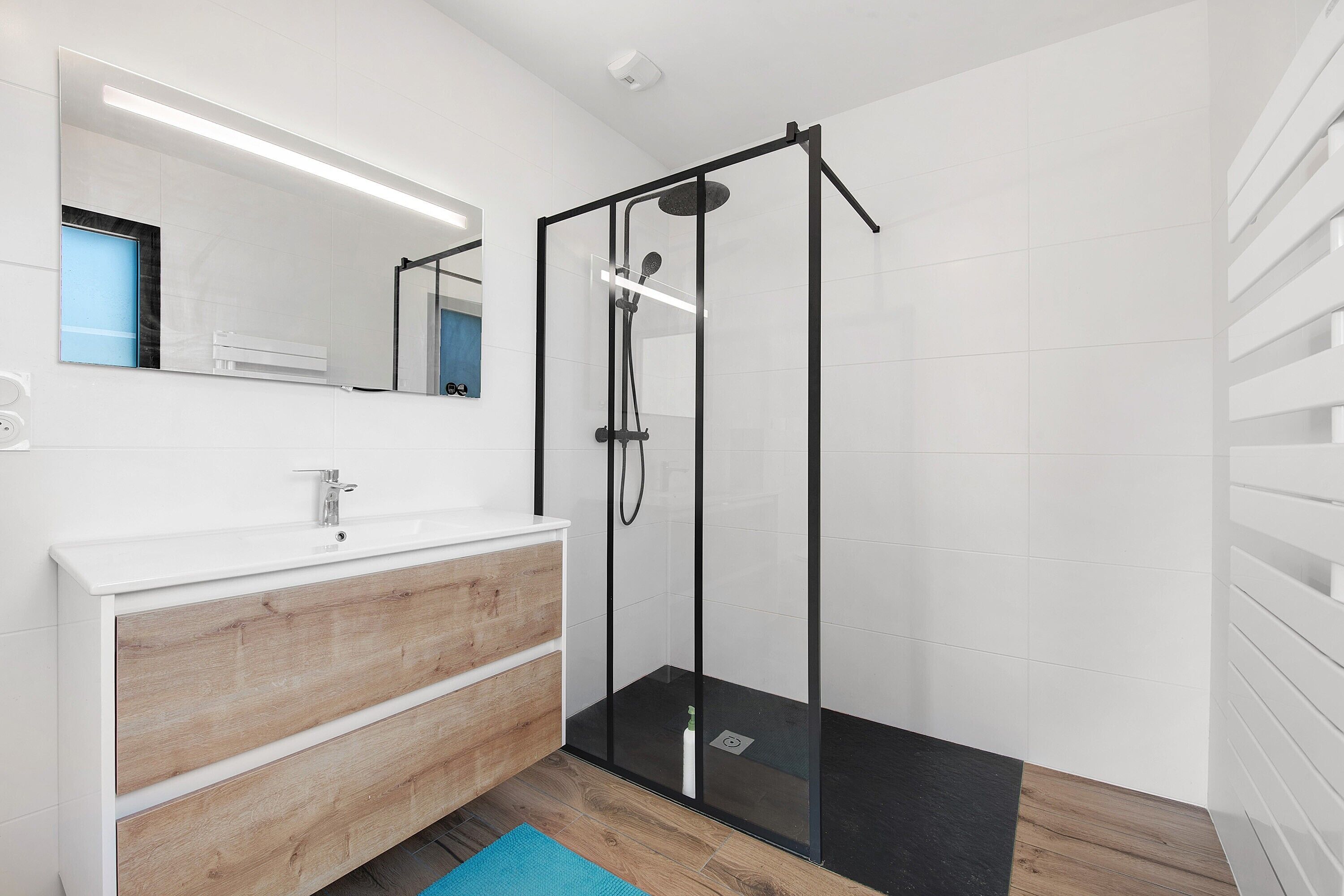 A modern bathroom with a glass-enclosed shower, a wooden vanity, and a large mirror.
