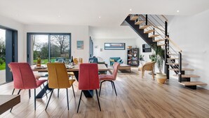 A modern interior with a dining area, a staircase, and a view through large windows. - Newly Built House for Rent! (Plouescat)