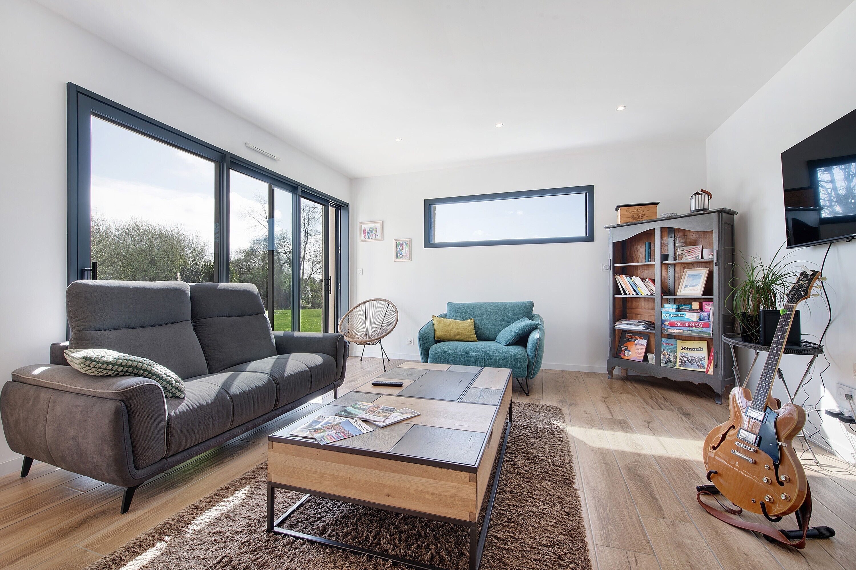 A modern living room with a sofa, coffee table, bookshelf, and a guitar.