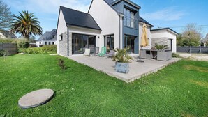 A modern two-story house with a large lawn, outdoor seating, and a stone facade. - Newly Built House for Rent! (Plouescat)