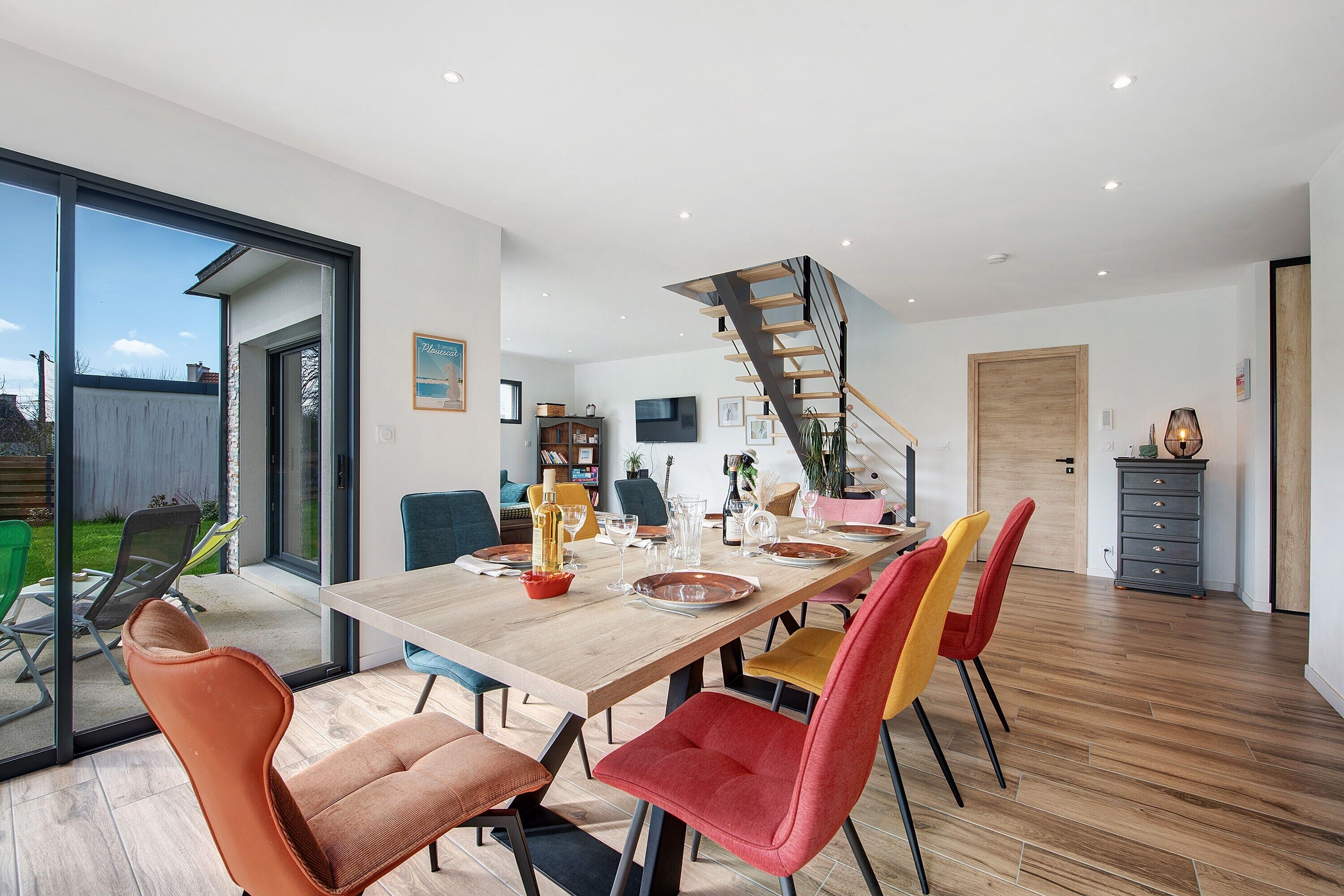 A dining area with a wooden table, colorful chairs, and a staircase leading to another level.