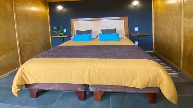 A wooden ceiling with a hanging light fixture, a bed with a headboard, two bedside tables, and a small potted plant. - Caba a Dormitorio Parking Wifi (Casablanca)