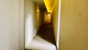 Un couloir étroit et faiblement éclairé, avec un plafonnier jaune.