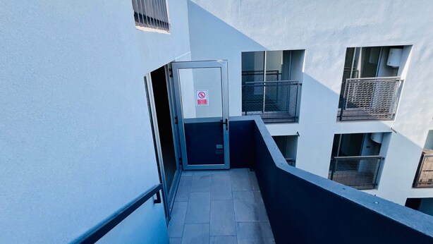 Un étroit couloir extérieur, doté d’une grille métallique, d’un panneau indiquant l’interdiction d’accès et d’un sol carrelé.