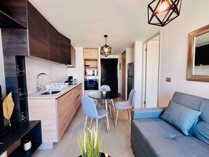 A modern kitchen with a dining area, a sofa, and a pendant light. - Urbano Santa Elena - Cowork Gym Parking Washer (Santiago)