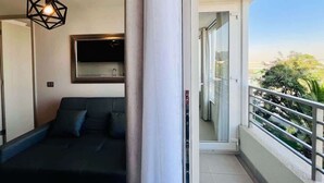 Un balcon donnant sur un espace verdoyant, un canapé noir et une suspension au design géométrique.