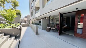 Een modern gebouw met een overdekt terras, trappen naar een balkon en buitenmeubels.