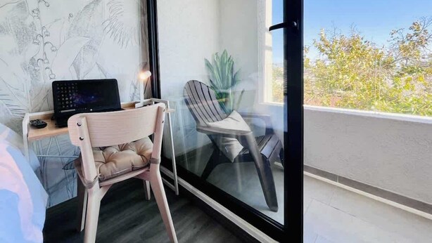 Een balkon met een laptop op een tafeltje, twee stoelen en een bloempot.
