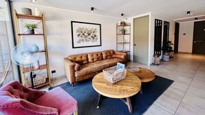 Een moderne woonkamer met een leren bank, twee houten salontafels, een roze fauteuil en een vloerlamp.