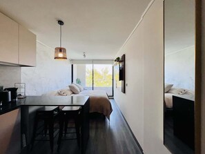 Un dormitorio moderno y compacto con un ventanal grande, una mesita de noche y una silla.