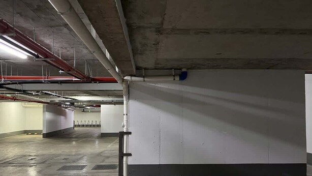 An empty parking garage with concrete floors and walls, visible pipes, and a clean, well-maintained environment. - Urbano Art Stico Irarr Zaval A C Laundry Parking (Santiago)