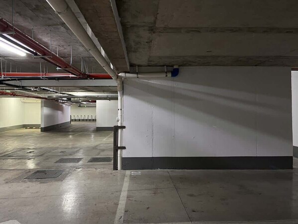 An empty parking garage with concrete floors and walls, visible pipes, and a clean, well-maintained environment. - Urbano Art Stico Irarr Zaval A C Laundry Parking (Santiago)
