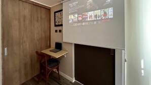 A small room with a wooden desk, a chair, and a projector screen displaying a Netflix interface. - Urbano Art Stico Irarr Zaval A C Laundry Parking (Santiago)