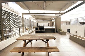 A covered outdoor patio with wooden tables and benches, a grill, and a view of the city. - Urbano Loft Panor Mico A C Laundry Pool Wifi (Santiago)