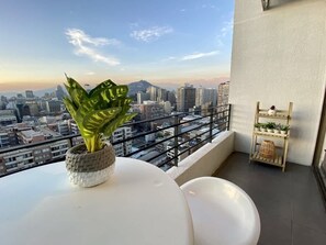 A balcony with a city view, a potted plant, a white table, and a wooden shelf with plants. - Urbano Loft Panor Mico A C Laundry Pool Wifi (Santiago)