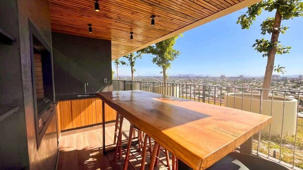 Een houten terras met een lange tafel en stoelen, met uitzicht op een stadsgezicht.