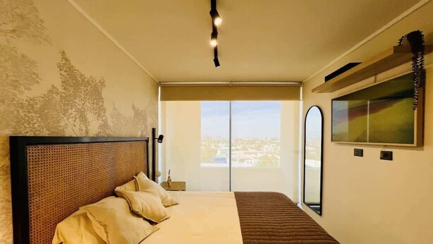 A bedroom with a large bed, a view of the city through a window, and a painting on the wall. - Buho Estudio Castillo Velasco B (Santiago)