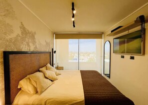 A bedroom with a large bed, a view of the city through a window, and a painting on the wall. - Buho Estudio Castillo Velasco B (Santiago)