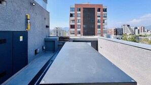 A rooftop terrace with a flat surface, a ventilation system, and a view of a cityscape with modern buildings. - Buho Estudio Castillo Velasco B (Santiago)