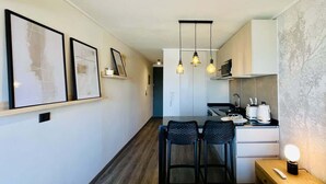 A modern kitchen with a dining area, featuring pendant lights, a wooden table, and a small bar area. - Buho Estudio Castillo Velasco B (Santiago)