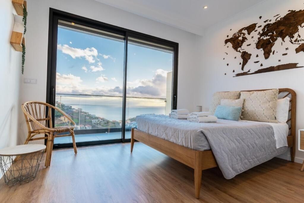 A bedroom with a large window, a bed with pillows, a chair, and a world map on the wall.