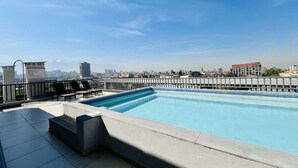 Ein Pool auf dem Dach mit Blick auf die Stadt, einer Steuerung und Liegestühlen.